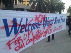 A banner reading "Welcome World Social Forum" over which has been spraypainted "ACAB" and "Forum du Capital"