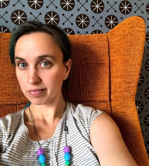 Image of sky sitting on a chair with some amazing 70s wallpaper behind her.